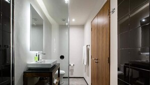 Un bagno moderno con cabina doccia in vetro, porta in legno e lavabo bianco con specchio.