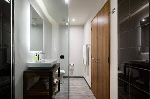 Ein modernes Badezimmer mit Duschkabine aus Glas, einer Holztür und einem weißen Waschbecken mit Spiegel.