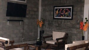 A room with a stone wall, a mounted television, a framed colorful artwork, and wooden furniture. - 3-bedroom house in amazing Darién with cool AC breeze (Darién)