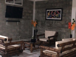 A room with a stone wall, a mounted television, a framed colorful artwork, and wooden furniture.