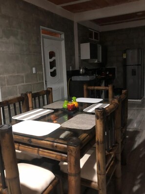 A dining area with a glass table, wooden chairs, and a kitchen in the background.