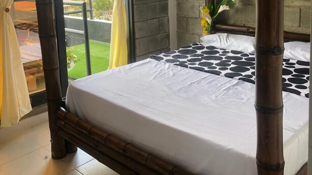 A bed with a white sheet, a view of the outdoors, and a bamboo bed frame. - 3-bedroom house in amazing Darién with cool AC breeze (Darién)