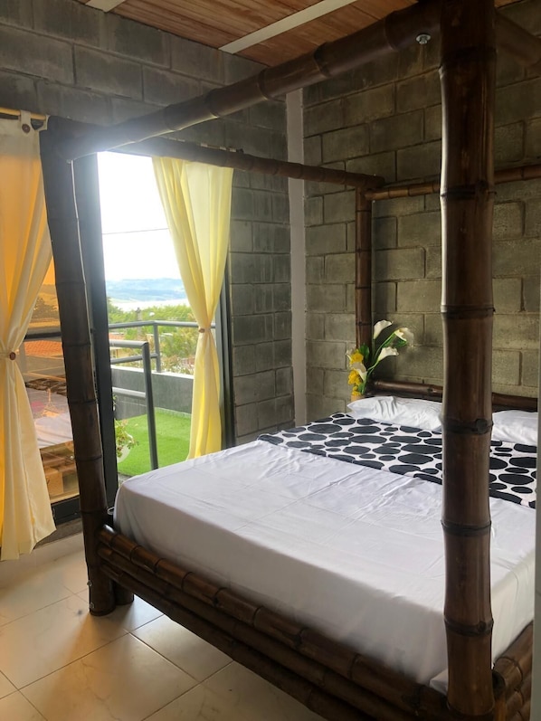A bed with a white sheet, a view of the outdoors, and a bamboo bed frame.