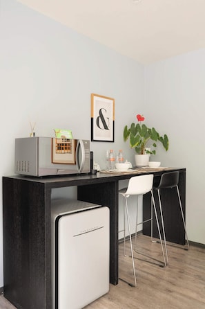 Eine moderne Küche mit Mikrowelle, Kühlschrank, Kaffeemaschine, einem Blumentopf und einem gerahmten Bild an der Wand.