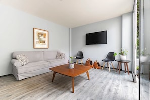 Ein modernes Wohnzimmer mit einer Couch, einem Couchtisch, einem Fernseher und einem großen Fenster.