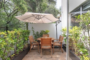 Eine Terrasse mit Tisch und Stühlen, umgeben von Pflanzen und einem großen Sonnenschirm.