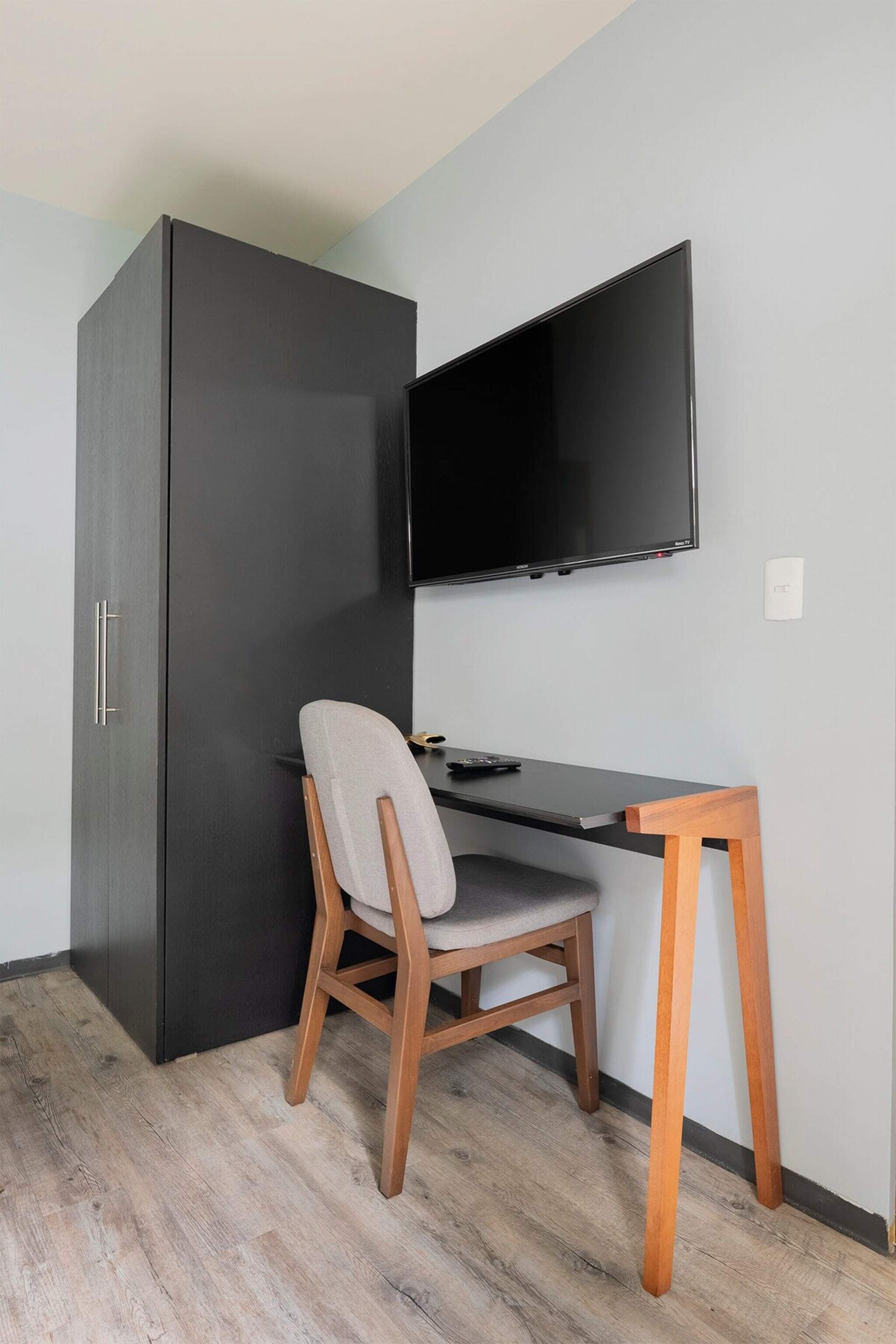 A room with a dark wardrobe, a desk with a chair, and a mounted TV.