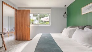 Quarto moderno com uma cama grande, porta de madeira, janela com vista e uma parede verde decorativa.