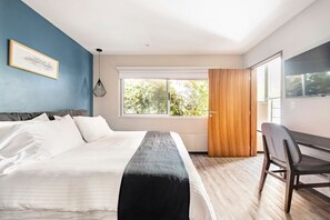 Ein Schlafzimmer mit Bett, Schreibtisch, Stuhl, Fenster und Tür.