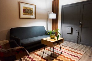 A living room with a dark sofa, a small wooden side table with a plant, a floor lamp, and a chevron-patterned rug. - Loft Con Terraza Privada en Corazon Polanco (Ciudad de México)
