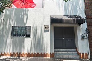 A building with a white exterior, a window with bars, a door with a nameplate, and a brick base. - Loft Con Terraza Privada en Corazon Polanco (Ciudad de México)
