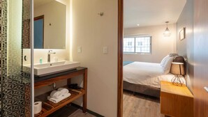 Ein Hotelzimmer mit Bad, einem Bett, einem Nachttisch mit Lampe und einem Fenster.