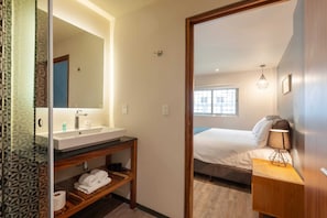 Ein Hotelzimmer mit Bad, einem Bett, einem Nachttisch mit Lampe und einem Fenster.