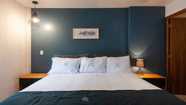 Ein ordentlich bezogenes Bett mit dunklem Kopfteil, ein gerahmtes Bild an der Wand und eine Nachttischlampe.