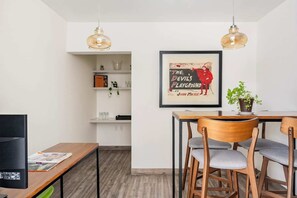 Ein moderner Essbereich mit Holztisch, Stühlen, Pendelleuchten, einem gerahmten Bild und einem Blumentopf.
