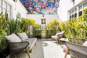 A patio with wicker furniture, potted plants, and a colorful mural on the wall.