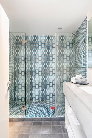 Un baño con baldosas estampadas, ducha y lavabo con toallas.