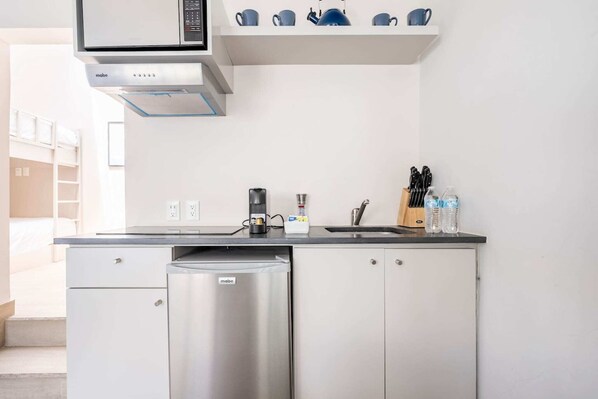 Una kitchenette compacta equipada con microondas, cafetera y un refrigerador pequeño.