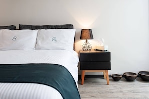 Ein ordentlich bezogenes Bett mit Kissen, ein Nachttisch mit Lampe und drei Schalen auf dem Boden.