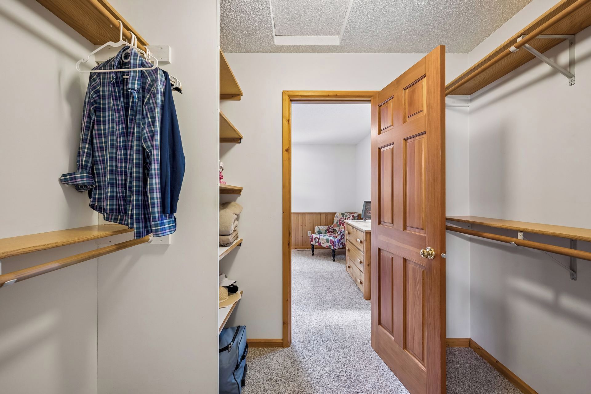 A hallway with a wooden door, a closet with shelves, and a hanging garment.