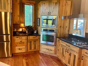 A kitchen with wooden cabinets, stainless steel appliances, and a window with a view of greenery. - Perfect house in peaceful Seeley Lake for a relaxing getaway (Seeley Lake)