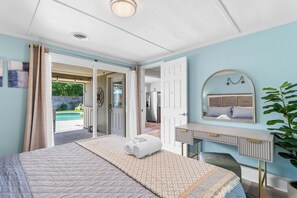 Ein Schlafzimmer mit Bett, Schreibtisch, Spiegel und Blick auf einen Pool.
