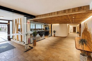 Un moderno vestíbulo de hotel con techo de madera, divisiones de vidrio y plantas en macetas.