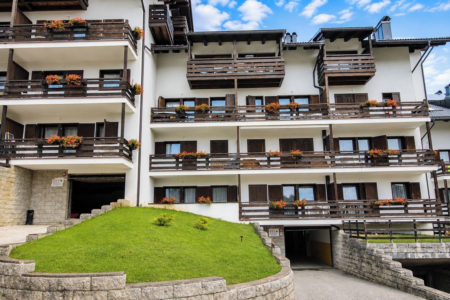Un hotel de varios pisos con balcones, fachada de piedra y una pequeña zona verde frente a él.