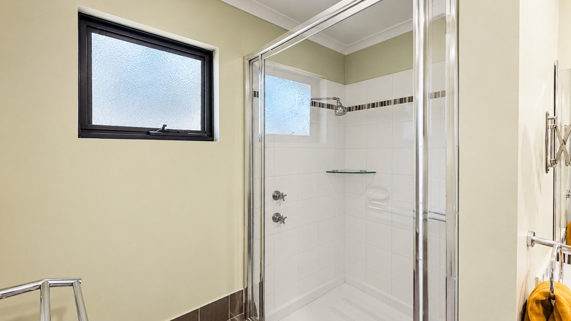 A glass-enclosed shower with a window, a towel rack, and a small shelf.