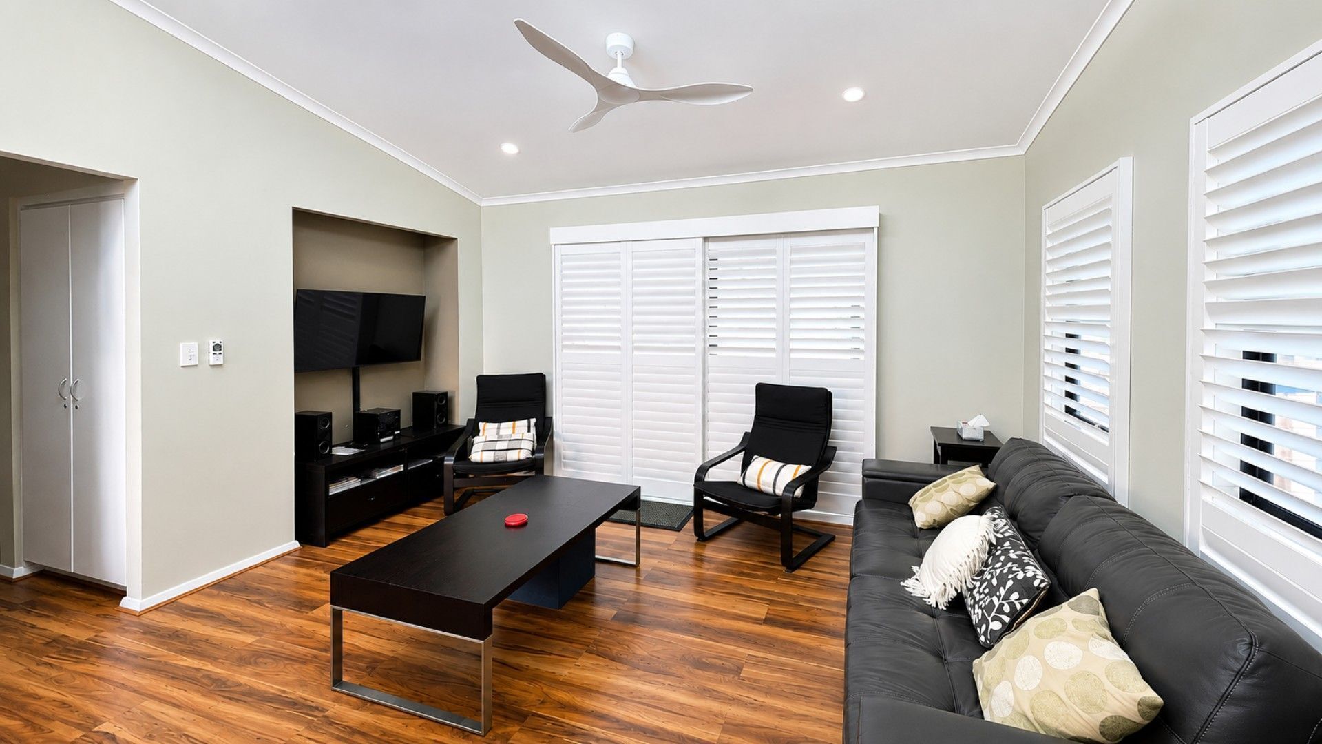 A modern living room with a flat-screen TV, a ceiling fan, a black sofa, a coffee table, and a TV stand.
