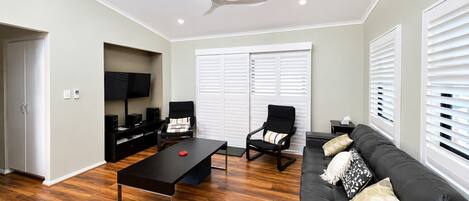 A modern living room with a flat-screen TV, a ceiling fan, a black sofa, a coffee table, and a TV stand.