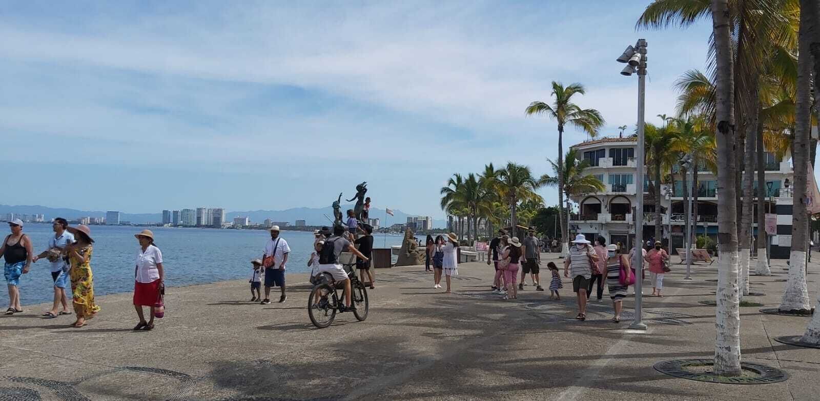 Un paseo marítimo con gente caminando, un ciclista y palmeras.