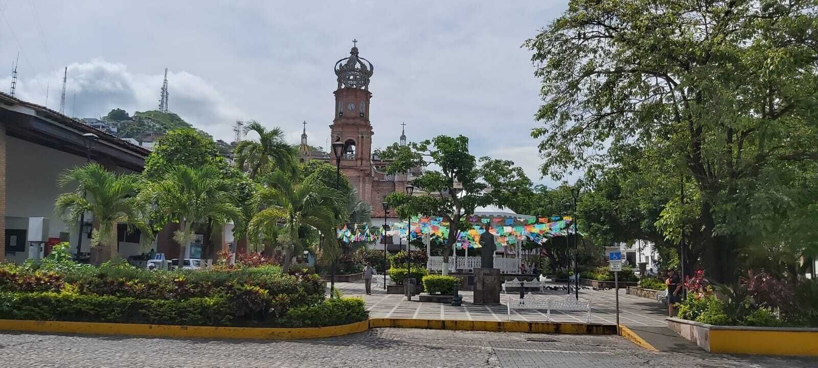 A plaza with a clock tower, palm trees, and a statue.
