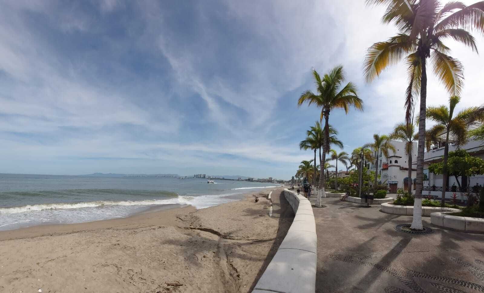 Ein Strand mit einer Betonpromenade, Palmen und Gebäuden im Hintergrund.