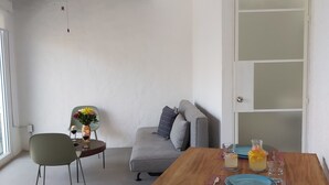Een moderne eetruimte met een houten tafel, groene stoelen, een grijze bank en een witte deur met geëtste glaspanelen.