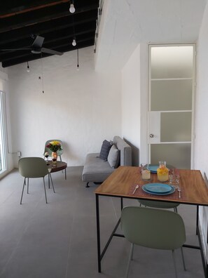 A modern dining area with a wooden table, green chairs, a grey sofa, and a white door with frosted glass panels. - Beautiful apartment with a view of the small town and just 10 minutes from the Romantic District. (Puerto Vallarta)