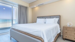 A hotel room with a large bed, a bedside table with a lamp, and a view of the beach. - Luxury beach front condo Viento 303 (Puerto Peñasco)