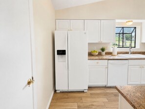 A kitchen with white cabinets, a double-door refrigerator, a granite countertop, and a window with a view of greenery. - Charming 2-bedroom townhome in Punta Gorda perfect for relaxing stay (Punta Gorda)