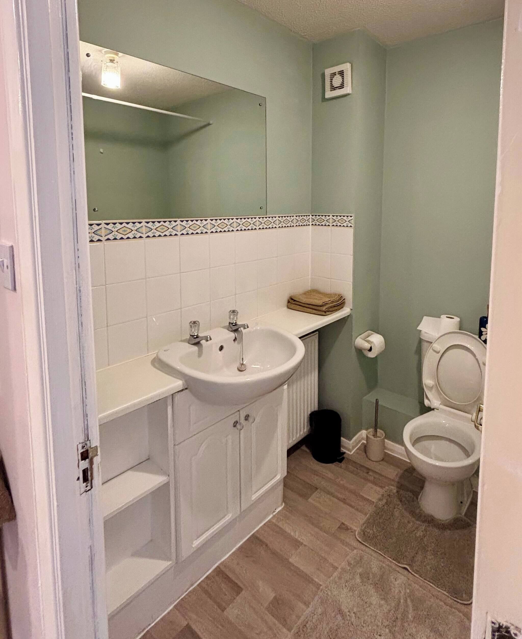 Ein Badezimmer mit Waschbecken, Spiegel, Toilette und einer kleinen Ablage mit Handtüchern.