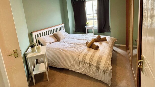 Un dormitorio con cama, mesita de noche y ventana con cortinas.