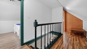 A room with a wooden floor, white walls, a green door frame, a black railing, and a wooden bench. - Doc's Place on Lark's:  Sleeps 4-Kayaks-Lakefront! (Pellston)