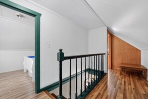 A room with a wooden floor, white walls, a green door frame, a black railing, and a wooden bench. - Doc's Place on Lark's:  Sleeps 4-Kayaks-Lakefront! (Pellston)
