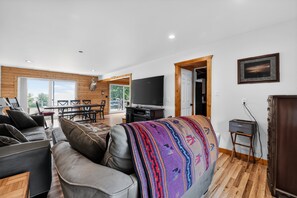 A modern living room with a sofa, television, and a dining area with a table and chairs. - Doc's Place on Lark's: Northern Michigan Ski Retreat | Lark's Lake | Near Nubs Nob (Pellston)