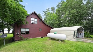 A red house with a white garage and a green lawn. - Doc's Place on Lark's:  Sleeps 4-Kayaks-Lakefront! (Pellston)