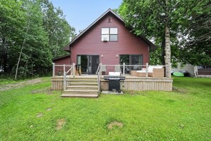 A red wooden house with a front deck, a grill, and a staircase leading to the door. - Doc's Place on Lark's:  Sleeps 4-Kayaks-Lakefront! (Pellston)