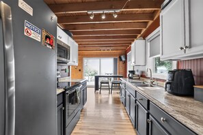 A modern kitchen with wooden beams, stainless steel appliances, and a large window. - Doc's Place on Lark's: Northern Michigan Ski Retreat | Lark's Lake | Near Nubs Nob (Pellston)