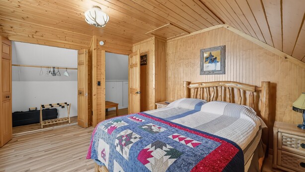 A wooden room with a bed, a wardrobe, and a hanging light fixture. - Doc's Place on Lark's:  Sleeps 4-Kayaks-Lakefront! (Pellston)