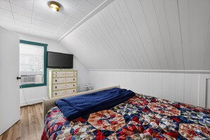 A bedroom with a sloped ceiling, a bed with a quilt, a dresser, and a television on the wall. - Doc's Place on Lark's: Tunnel of Trees Getaway | Lark's Lake | Lakefront | 2BR (Pellston)