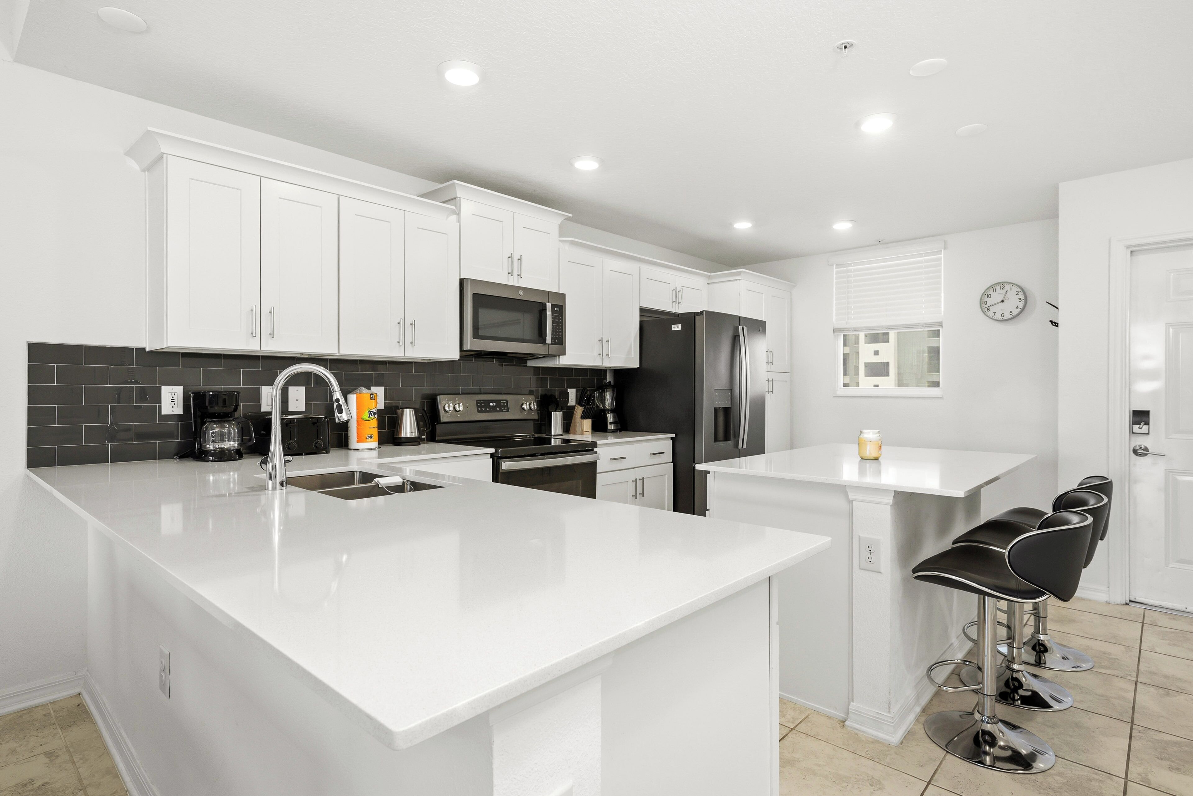 A modern kitchen with white cabinetry, stainless steel appliances, a large island, and bar stools.