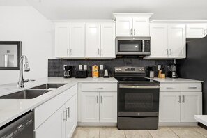 Eine moderne Küche mit weißen Schränken, einer Edelstahl-Mikrowelle, einem schwarzen Backofen und einem Geschirrspüler.